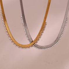 Elevate your look with the Gleaming Edge Herringbone Necklace. Available in both 18-karat yellow gold and 18-karat white gold finishes, this stunning piece is crafted from durable titanium steel. The herringbone chain, adorned with a dazzling array of clear zircons, shimmers beautifully in any light. Perfect for layering or wearing solo, this necklace adds a touch of elegance and sparkle to your ensemble. Whether you choose gold or silver, the Gleaming Edge Herringbone Necklace is your new go-to for a chic and radiant style. Luxury Stainless Steel Necklace With Adjustable Chain, White Gold Metal Necklace Tarnish Resistant, Elegant Silver Herringbone Necklace With Adjustable Chain, Modern White Gold Snake Chain Necklace, Tarnish Resistant White Gold Chain Necklace, Tarnish Resistant White Gold Metal Chain Necklace, Luxury Metal Snake Chain Necklace, Tarnish Resistant White Gold Metal Necklace, Elegant Silver Chain Tennis Necklace