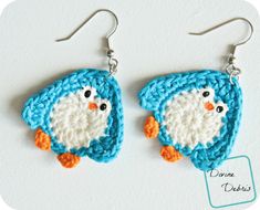 a pair of crocheted penguin earrings with orange beaks and white wings, hanging from silver earwires