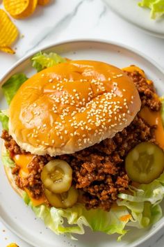 a sloppy joe sandwich with pickles and cheese on a white plate next to chips