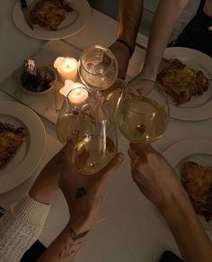 several people toasting wine glasses at a dinner table with food and candles in the background