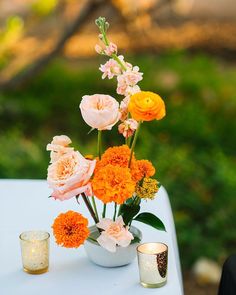 an arrangement of flowers in a white vase on a table with two votive candles