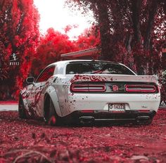 a white car with red paint on it parked in front of some trees and leaves