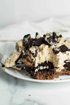 a white plate topped with cake covered in oreo cookies and cream frosting next to a fork