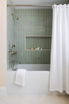 a bath tub sitting under a bathroom window next to a white shower curtain and tiled walls