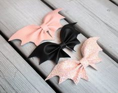 three bows with black and pink glitters are sitting on a wooden surface, one has a large bow at the top