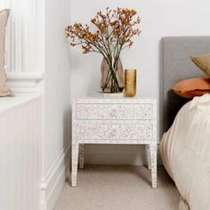 a white nightstand with flowers on it next to a bed