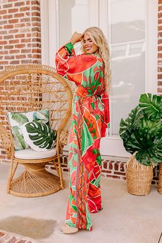 - This stunning jumpsuit is a ticket to sunshine vibes! Featuring a bold vibrant print and a chic satin finish, this trendy wide leg jumpsuit promises to steal the spotlight and keep you feeling fabulous. - Unlined material with a pink, orange, and green hued abstract botanical print with a satin finish - A v-cut neckline and a v-cut back with a tie detail - Long. loose sleeves - A waistline with an elastic back and an attached tie closure belt - A relaxed silhouette that ends in wide hemlines Chic Orange Jumpsuits And Rompers For Vacation, Chic Orange Jumpsuit And Romper For Vacation, Bohemian Maxi Length Jumpsuits And Rompers For Party, Trendy Orange Jumpsuits And Rompers For Beach, Orange Floral Print Jumpsuit For Vacation, Orange Floral Print Jumpsuits And Rompers For Vacation, Beach Multicolor Maxi Jumpsuits And Rompers, Multicolor Maxi Length Jumpsuits And Rompers For Vacation, Multicolor Maxi Length Jumpsuits And Rompers For Beach