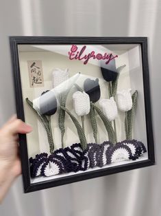 a person holding up a frame with crocheted flowers in it