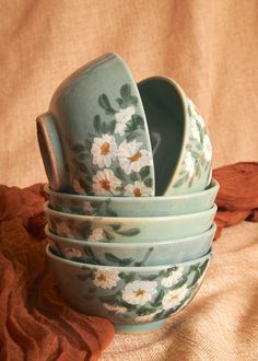 a stack of ceramic dishes with flowers painted on the front and sides, sitting on a brown cloth