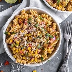 two bowls filled with pasta salad next to silverware and lime wedges on the side