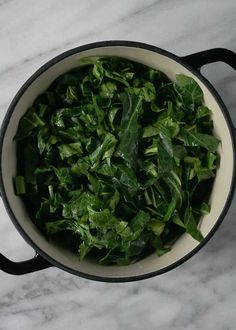 a pot filled with greens on top of a marble counter