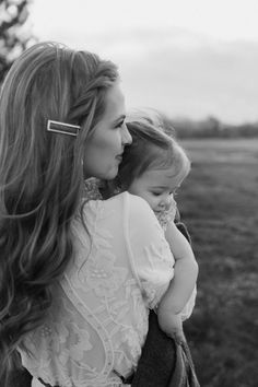 a woman holding a child in her arms and looking at the sky with long hair