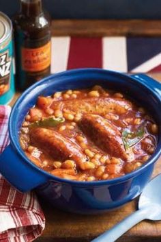 a blue bowl filled with beans and meat on top of a wooden table next to two bottles