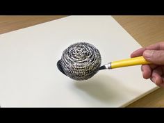 a person is holding a pencil and drawing a ball with silver filigrees