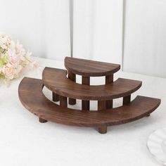 three tiered wooden trays sitting on top of a white table next to flowers