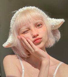 a woman with white hair and horns on her head is posing for the camera while holding her hand to her face