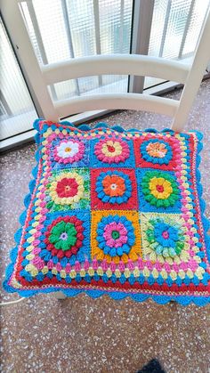 a crocheted granny granny blanket sitting on top of a white chair next to a window