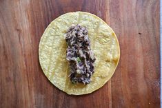 a tortilla with meat and sauce on it sitting on a wooden table next to a knife