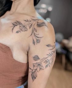 a woman wearing a brown top with leaves on her shoulder and arm tattooing it's upper half