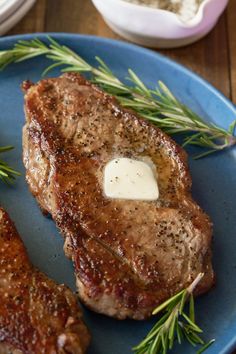 two pieces of steak on a blue plate with rosemary sprigs next to it