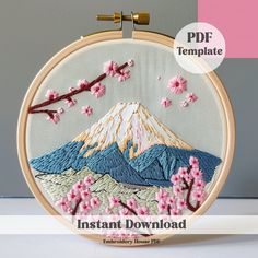 an embroidery pattern with pink flowers and a mountain in the background on a wooden hoop