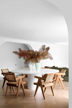 a white table with chairs around it and a vase filled with flowers in the center