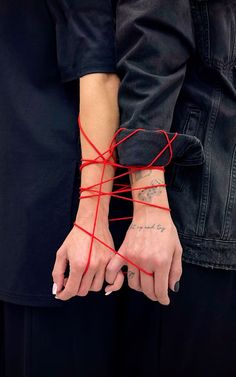 two people are holding hands with red string attached to their wrists and one is wearing a black jacket