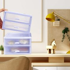 a person holding an open plastic storage box on top of a desk next to a chair