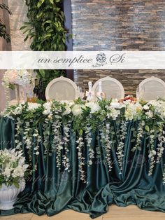 an arrangement of flowers and greenery is displayed on a table with green cloths