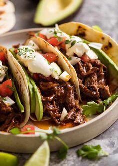 three shredded beef tacos with avocado and sour cream on top in a bowl