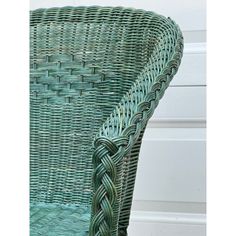 a green wicker chair with braiding on the back and seat, in front of a white wall