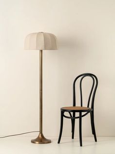 a chair next to a lamp on a white floor with a wall in the background