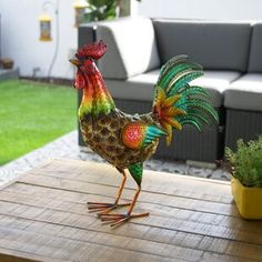 a colorful rooster figurine sitting on top of a wooden table next to a potted plant