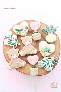 decorated cookies on a wooden plate with pink and green accents are arranged in the shape of teddy bears