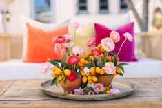 an arrangement of flowers on a tray in front of a bed with pillows and throw pillows