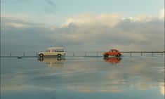 two cars are parked on the beach in front of an overcast sky and water