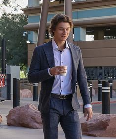 a man in a suit and tie walking down the street with a cup of coffee