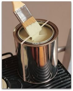 a paintbrush is being used to brush the interior of a metal can on top of a stove