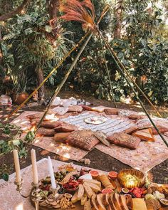 an outdoor picnic with food and candles on the ground in front of it, surrounded by greenery