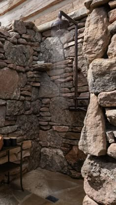 an outdoor shower with rocks and a bench in the corner, next to a stone wall