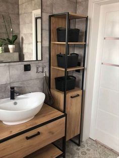 a bathroom sink sitting under a mirror next to a wooden shelf filled with black baskets