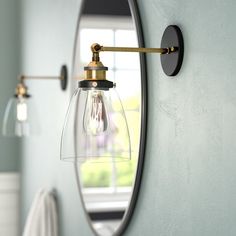 a bathroom mirror and light fixture in front of a wall mounted vanity lamp with an oval glass shade