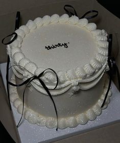 there is a white cake with black ribbon on the top and it's in a box