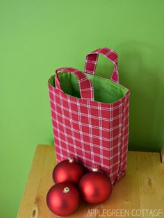 three red ornaments sitting on top of a wooden table next to a shopping bag and some green wall