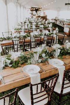 the tables are set up with white plates and greenery for an elegant wedding reception