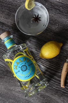 a bottle of alcohol sitting next to a glass and lemons on a wooden table