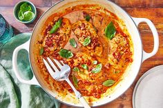 a pan filled with meat covered in sauce and garnished with basil leaves on top