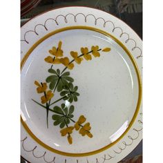 a white plate with yellow and green flowers painted on the side, sitting on a table