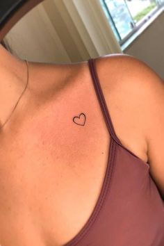 a woman with a small heart tattoo on her upper arm and chest is looking into the mirror