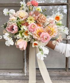 a bridal bouquet in front of a window with white ribbon and flowers on it